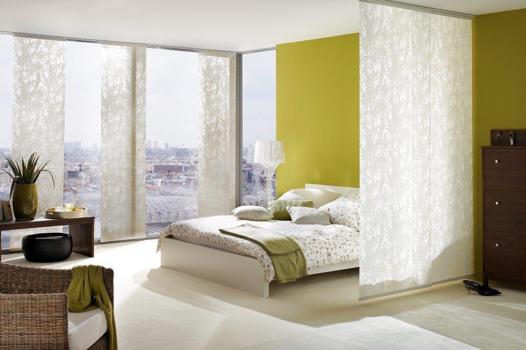 Helles, modernes Schlafzimmer mit transparenten und floralen Flächenvorhängen und Stadtpanorama. Foto von Germania.